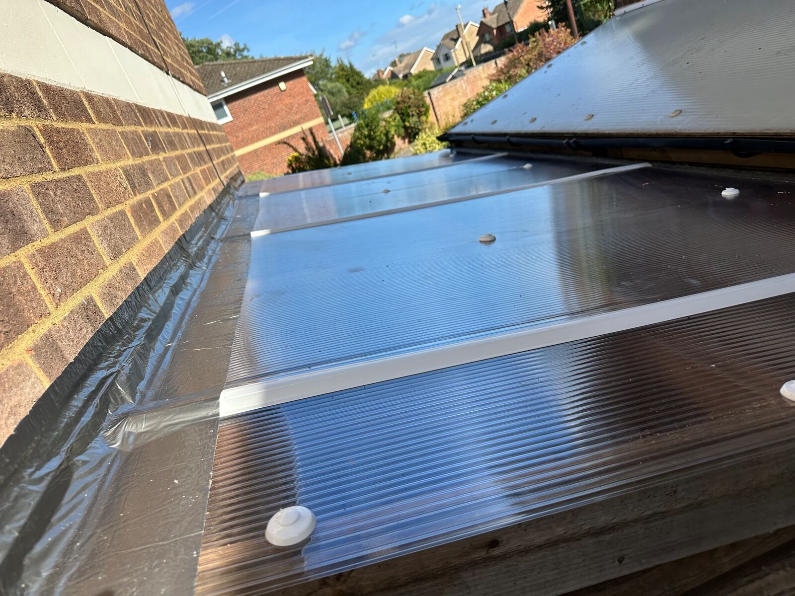 Close-up of polycarbonate roof sheets, glazing profile and butyl flashing tape where the lean-to roof meets the brick wall