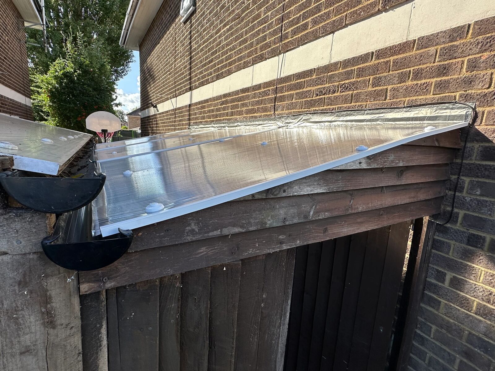 Side view of the completed polycarbonate lean-to roof showing the roof edge, guttering and Soudal Butyband flashing against the brick wall