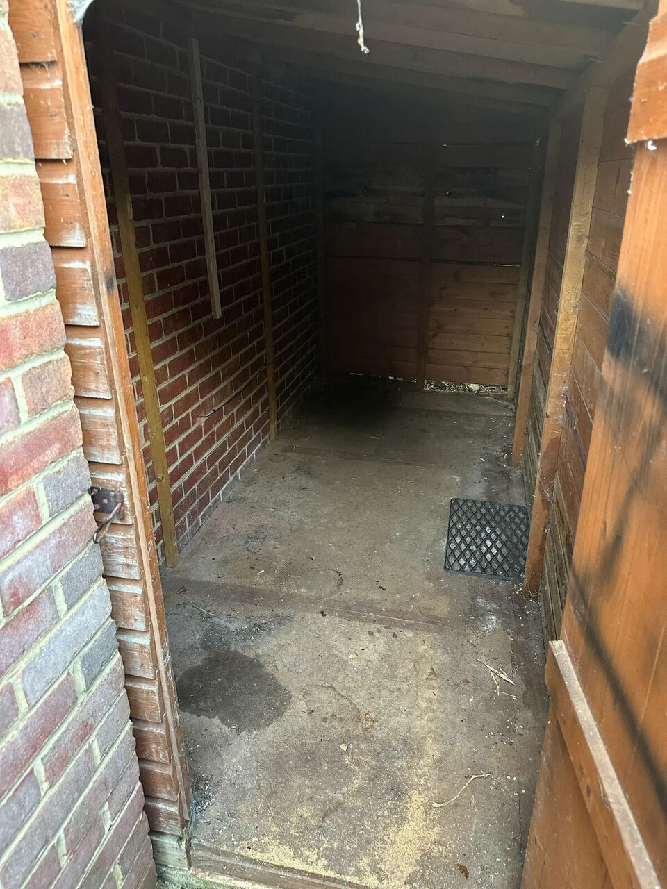 Inside the lean-to showing the original dark, water-damaged chipboard floor before replacement